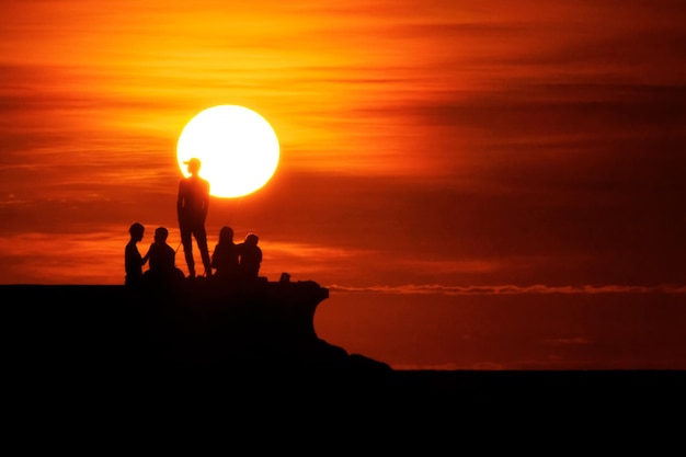 les gens regardent le coucher du soleil sur la plage