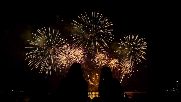 Les gens regardent ensemble de beaux feux d'artifice au bord de la mer pendant la nuit.