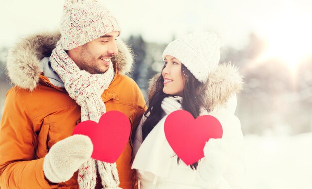 Photo les gens, la saison, l'amour et le concept de la saint-valentin - un couple heureux tenant des cœurs rouges vides sur le paysage hivernal