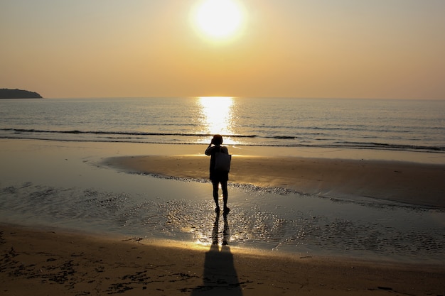 Gens de silhouette debout sur la plage au lever du soleil avec de l&#39;eau de mer magnifique
