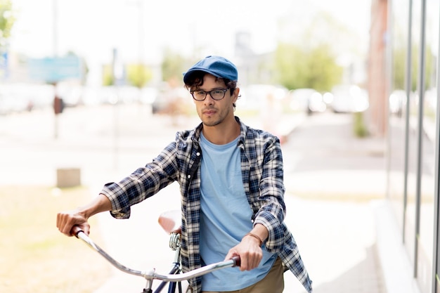 les gens, le style, la vie urbaine et le style de vie - jeune homme hipster en casquette vintage et vélo à pignon fixe marchant le long de la ville dans la rue