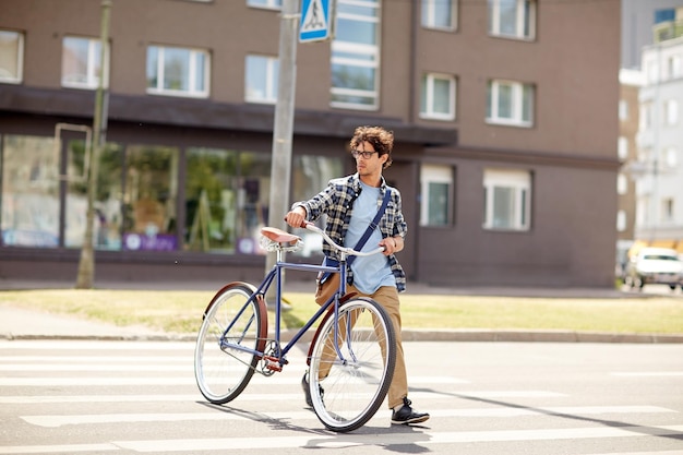 les gens, le style, la vie urbaine et le style de vie - jeune homme hipster avec sac à bandoulière et vélo à pignon fixe traversant le passage pour piétons dans la rue