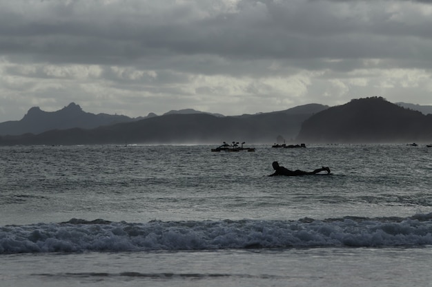 Photo les gens surfant à la plage avec des nuages