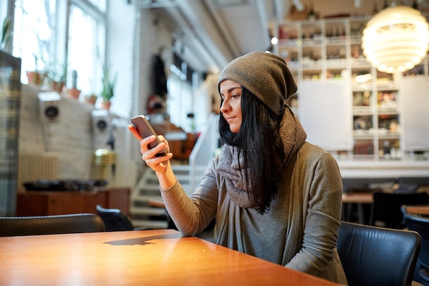 Les gens, la technologie et le concept de style de vie - une jeune femme souriante avec un smartphone dans un café