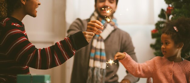 Des gens tenant des étincelles éclairées alors qu'ils se tiennent contre l'arbre de Noël