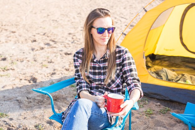 les gens, le tourisme d'été et le concept de la nature - jeune femme assise près de la tente