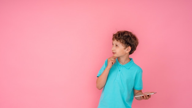 Gentil garçon tient le smartphone dans ses mains et regarde ailleurs sur rose.