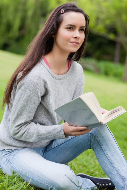 Gentil jeune femme tenant un livre assis sur l&#39;herbe