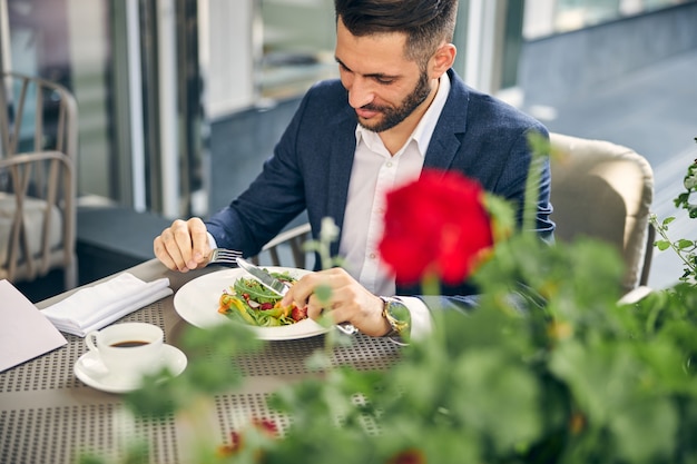 Gentil jeune homme gardant le sourire sur son visage tout en regardant une salade colorée