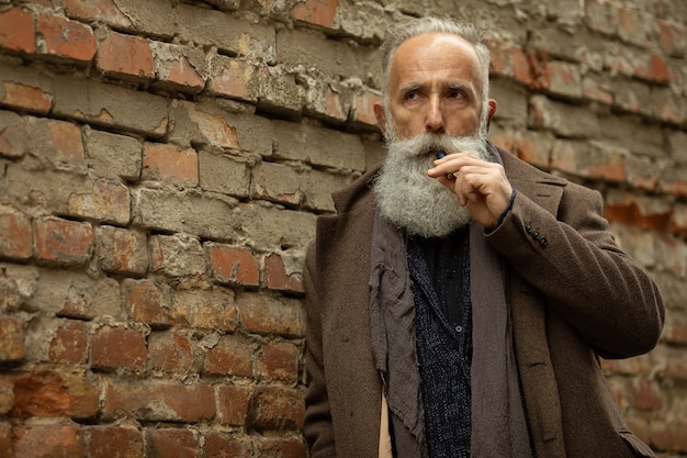 Gentilhomme élégant avec une longue barbe fumant en plein air.