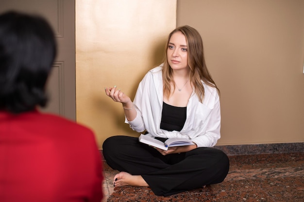 Une gentille fille psychologue reçoit un client assis par terre avec un journal