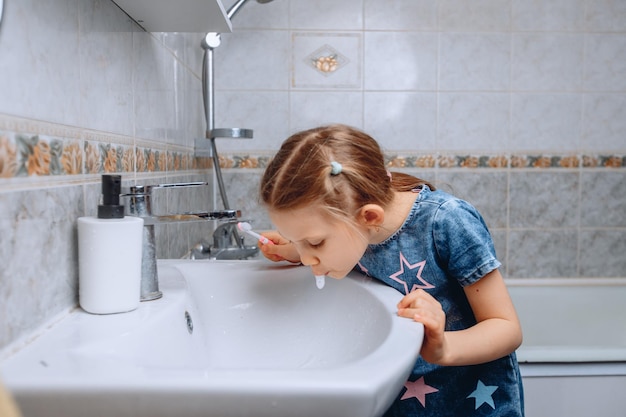 Une gentille petite fille de 6 ans termine son brossage de dents du matin en crachant de la pâte dans l'évier