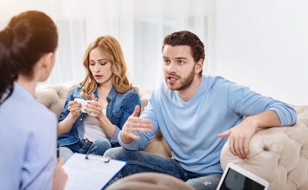 Gérer des problèmes. Déprimé malheureux jeune couple ayant un rendez-vous avec un psychologue et lui décrivant leurs problèmes tout en cherchant une solution