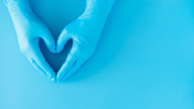 Geste des mains du médecin portant des gants bleus sur bleu, signe en forme de coeur pour l'amour