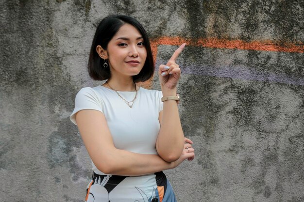 Photo geste de pensée d'une belle fille asiatique pointant à côté d'une chemise blanche