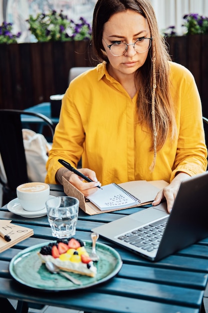 Gestion du temps pour les pigistes femme pigiste écrit dans un cahier et travaille avec un ordinateur portable