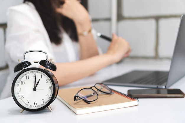 Gestion du temps, réveil noir avec femme d&#39;affaires brouillée travaille avec un ordinateur portable.