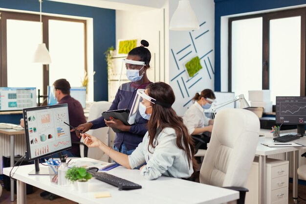 Gestionnaire africain donnant une indication à un employé sur le lieu de travail portant un masque facial agasint covid19. Équipe diversifiée travaillant dans le respect de la distanciation sociale pendant la pandémie mondiale de coronavirus. Nouvelle normalité.