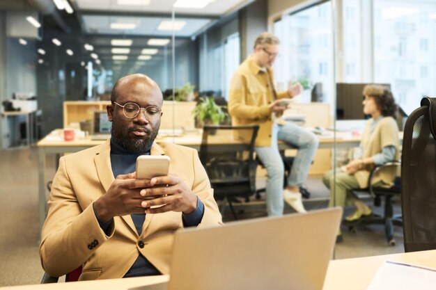 Gestionnaire afro-américain sérieux utilisant un smartphone sur le lieu de travail