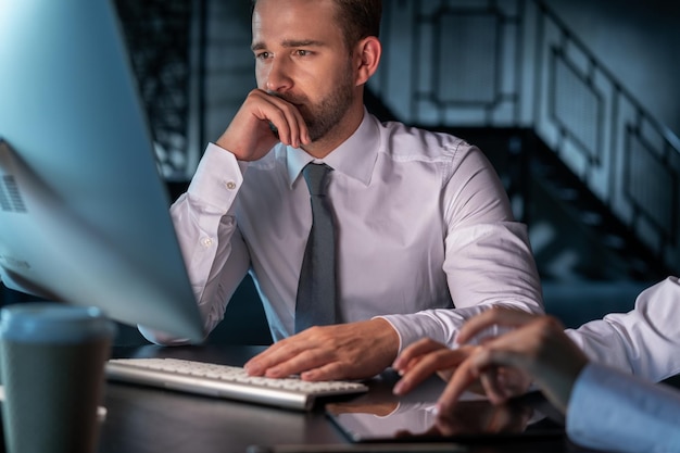 Gestionnaire de bureau homme pensant devant les mains de l'écran d'ordinateur sur le clavier Gestionnaires masculins et féminins en chemises blanches travaillant au bureau tard dans la nuit Concept de travail d'équipe