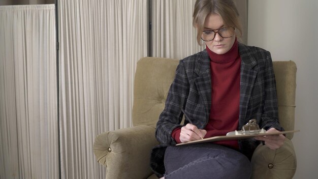 Gestionnaire féminin dans des lunettes dans la chaise prenant des notes en papier