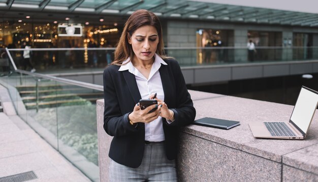 Gestionnaire féminine inquiète vêtue de vêtements de travail fronçant les sourcils et bavardant sérieusement sur un smartphone