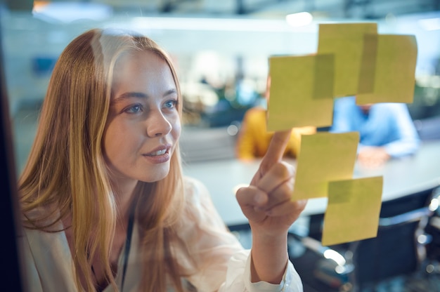 Photo la gestionnaire féminine regarde les feuilles de rappel, le bureau informatique. travailleur professionnel, planification ou remue-méninges. une femme d'affaires prospère travaille dans une entreprise moderne