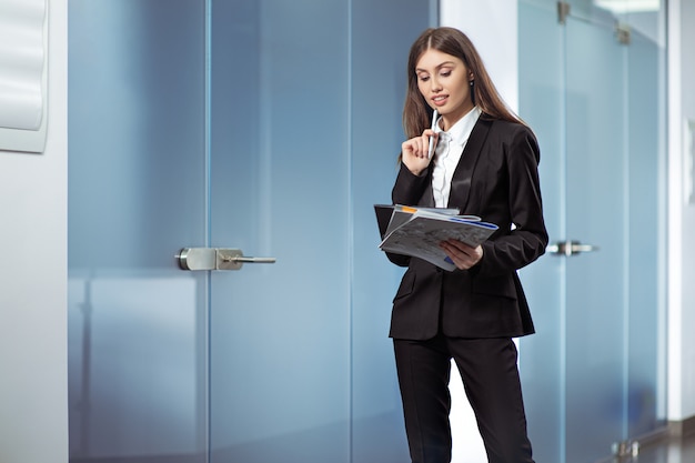 Gestionnaire de femme heureuse debout dans l'intérieur de bureau moderne, jeune femme secrétaire intelligente.