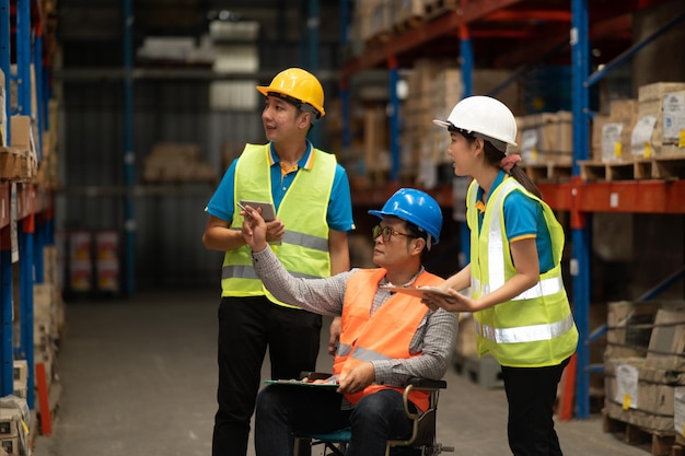 Gestionnaire handicapé en fauteuil roulant homme employé utilisant une tablette vérifier le travail de stock à l'entrepôt Travailleur portant des vêtements à haute visibilité et un casque de sécurité et vérifiant le comptage des boîtes de marchandises pour la livraison