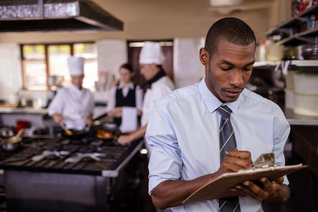 Photo gestionnaire mâle écrit sur un clipbaord dans la cuisine