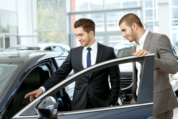 Gestionnaire de salon de voiture invitant le jeune client d'affaires à regarder à l'intérieur de la voiture