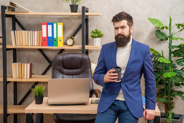 Gestionnaire sérieux en costume buvant du thé ou du café assis sur une pause de bureau