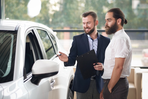 Gestionnaire souriant du centre de voiture montrant à l'homme brutal auto.