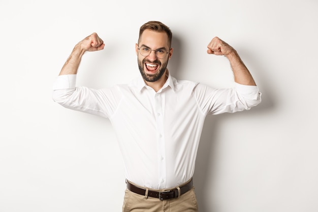 Gestionnaire de succès flex biceps, montrant les muscles et l'air confiant, debout sur fond blanc.