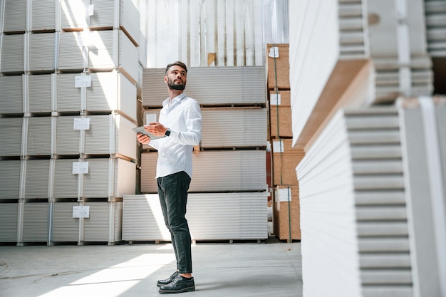 Le gestionnaire vérifie les données à l'aide d'une tablette Le travailleur du stockage est dans l'entrepôt avec un tas de produits