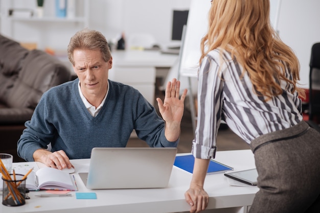 Gestionnaires de bureau matures et perplexes impliqués assis dans le bureau et exprimant des émotions négatives tout en travaillant et en discutant du projet