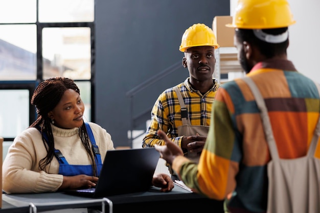 Gestionnaires d'entrepôt planifiant l'inventaire des marchandises au comptoir de réception. Superviseuse afro-américaine tapant sur un ordinateur portable et écoutant l'employé d'entrepôt expliquer le système de stockage des colis
