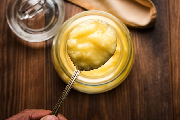 Ghee ou beurre clarifié en gros plan dans un bol en bois et une cuillère en argent, mise au point sélective