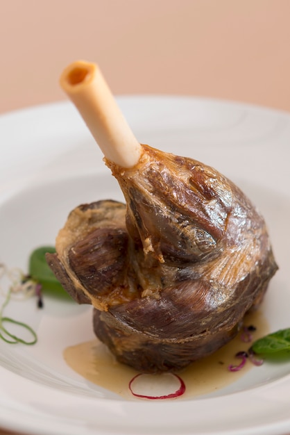 Photo gigot d'agneau rôti, servi avec une sauce blanche, décoré avec des herbes