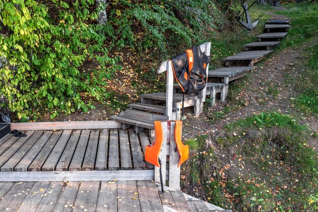 Des gilets de sauvetage sèchent sur les balustrades d'un escalier en bois sur la rive de la rivière.