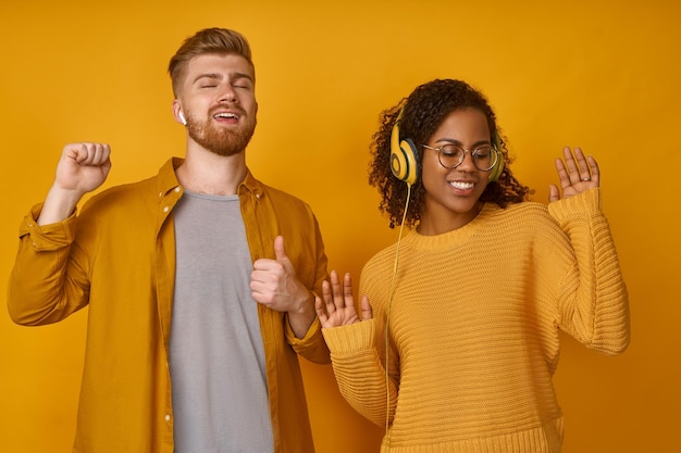 Gingembre énergisé mâle femelle noire danse joyeusement sourire largement tourner à l'appareil photo porte des écouteurs