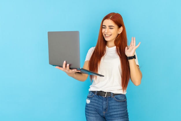 Gingembre Femme Assise étage Parler Ordinateur Portable En Agitant L'espace Bras Isolé Sur Bleu