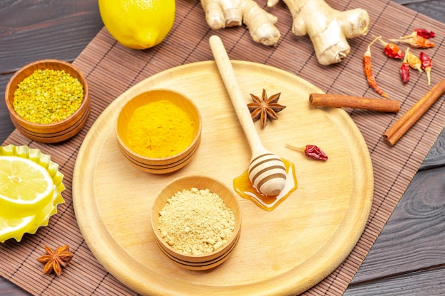 Gingembre sec et poudre de curcuma dans des bols, coller avec du miel. Bâtons de cannelle, racine de gingembre sur table. Fond en bois sombre. Vue de dessus