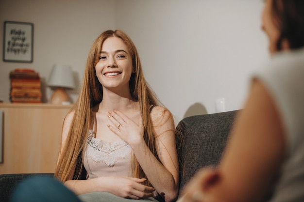 Ginger caucasian lady raconte une histoire intéressante à sa fille brune tout en se montrant et assise sur un canapé