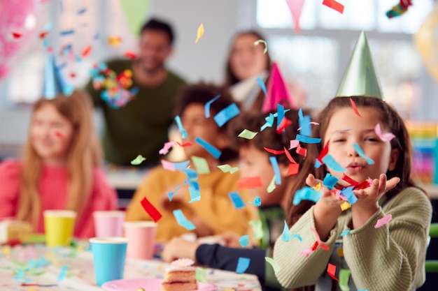 Girl Blowing Confetti At Camera à la fête d'anniversaire avec des amis et des parents à la maison