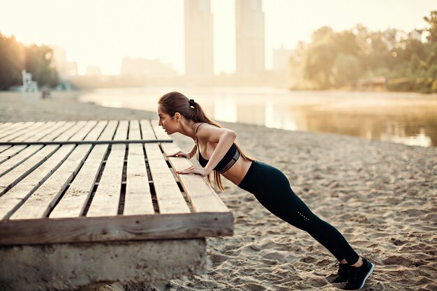 Girl do push ups sur plate-forme en bois sur la plage de la rivière