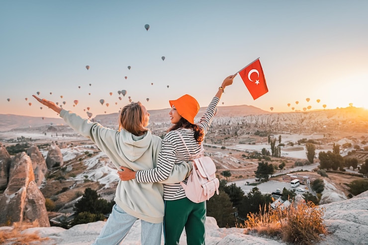 Photo girl friends voyageurs avec drapeau turc serrant sur un point de vue et admirant la vue de voler des ballons à air chaud en cappadoce
