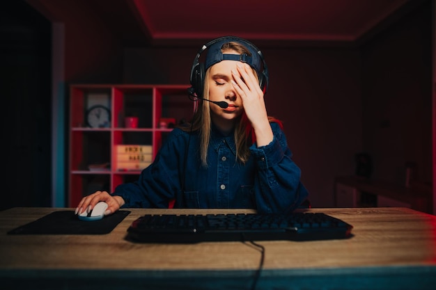 girl gamer est assis la nuit devant l'ordinateur et montre un geste de facepalm baissant les yeux