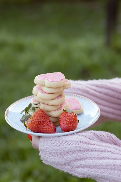 Girl holding plate avec des cookies en forme de coeur rose accompagnés de fraises