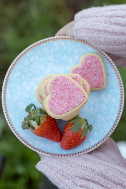 Girl holding plate avec des cookies en forme de coeur rose accompagnés de fraises